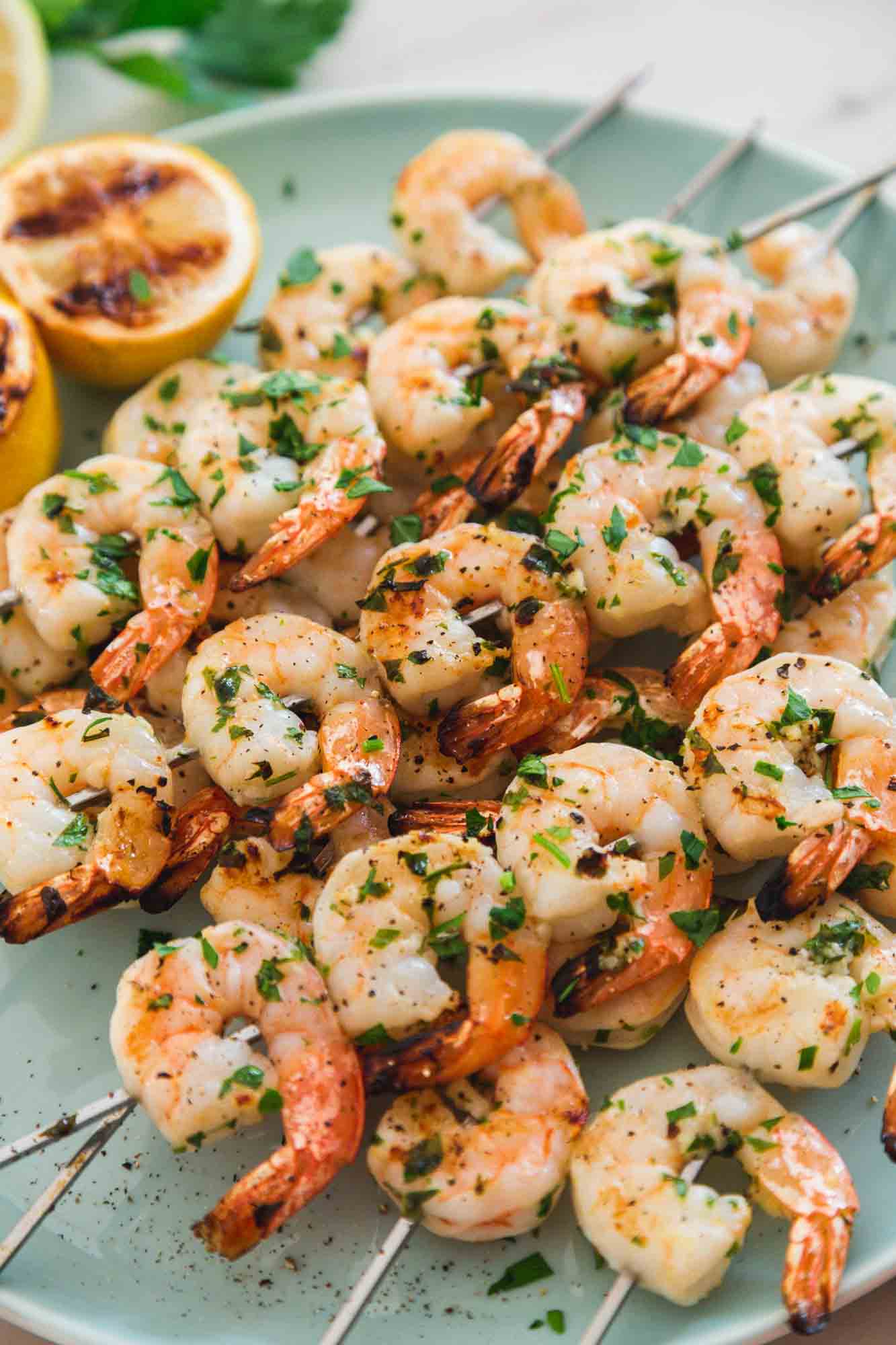Grilled shrimp skewers served on a blue platter with grilled lemons, and chopped parsley
