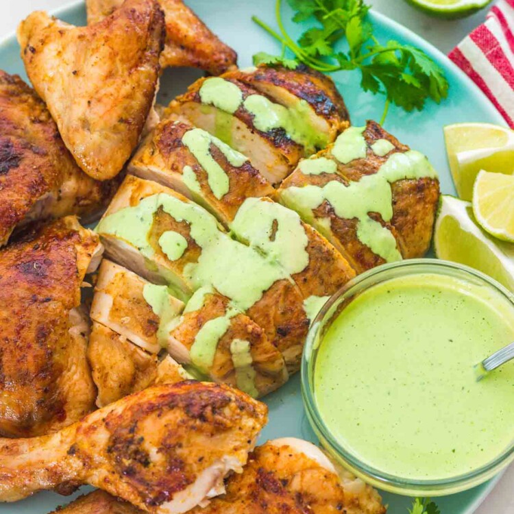 Carved Peruvian chicken on a plate with aji verde sauce on the side