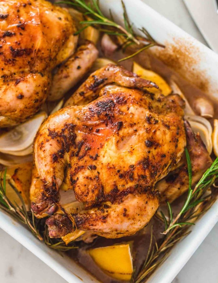 Overhead shot of two Cornish Hens in a roasting pan with rosemary and lemon