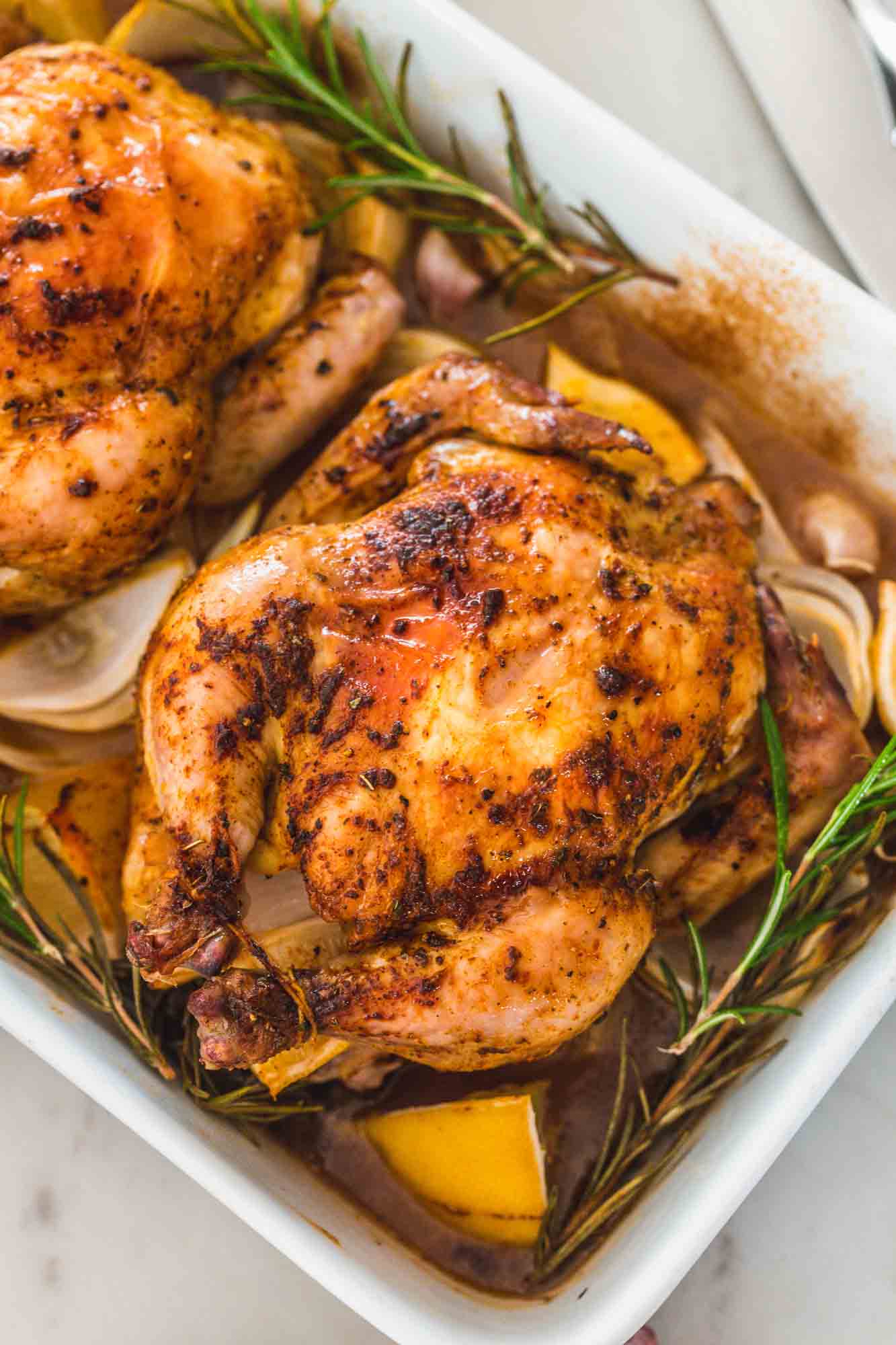 Overhead shot of two Cornish Hens in a roasting pan with rosemary and lemon