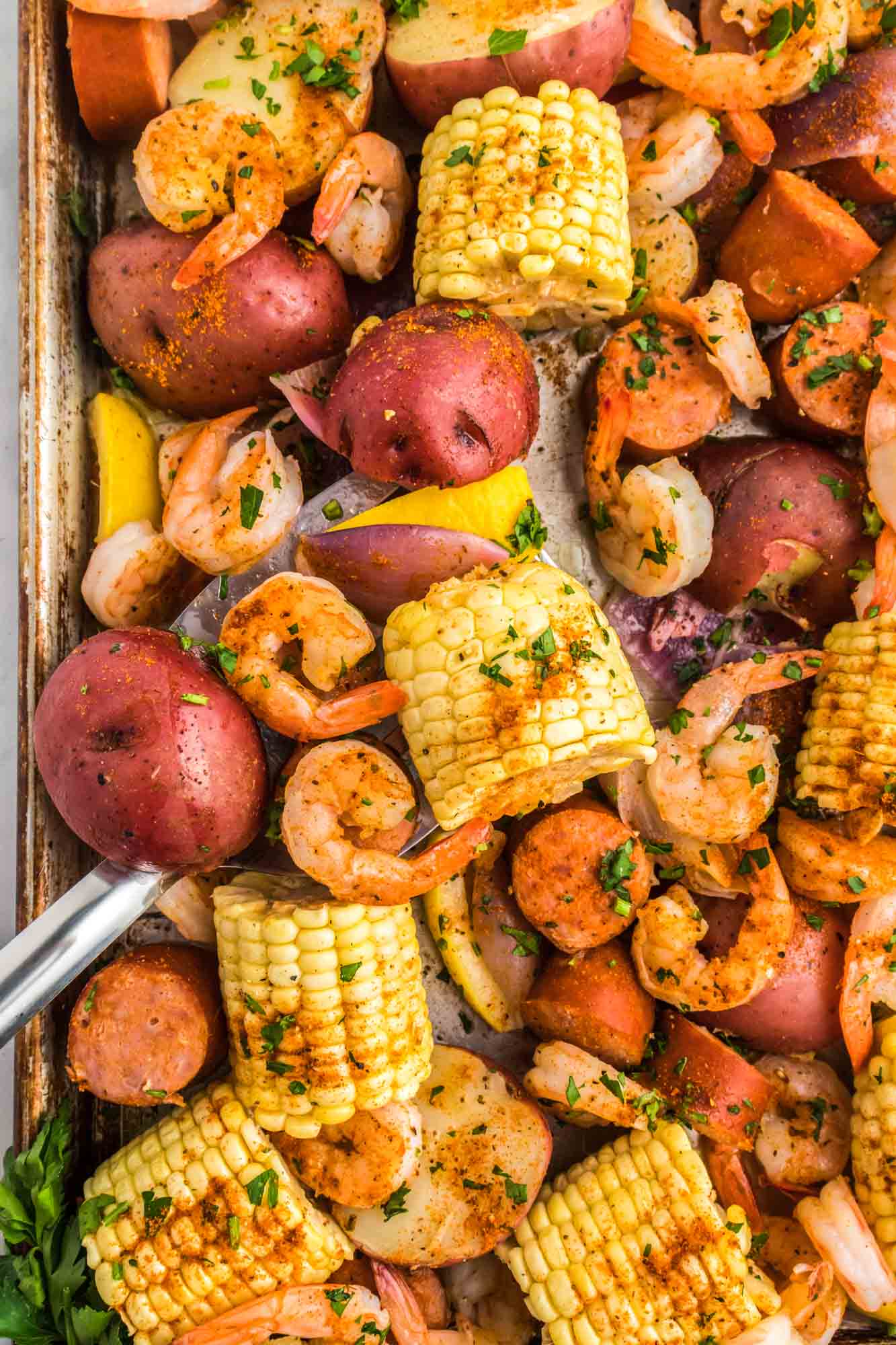 Overhead shot of shrimp boil on a sheet pan, garnished with fresh parsley leaves