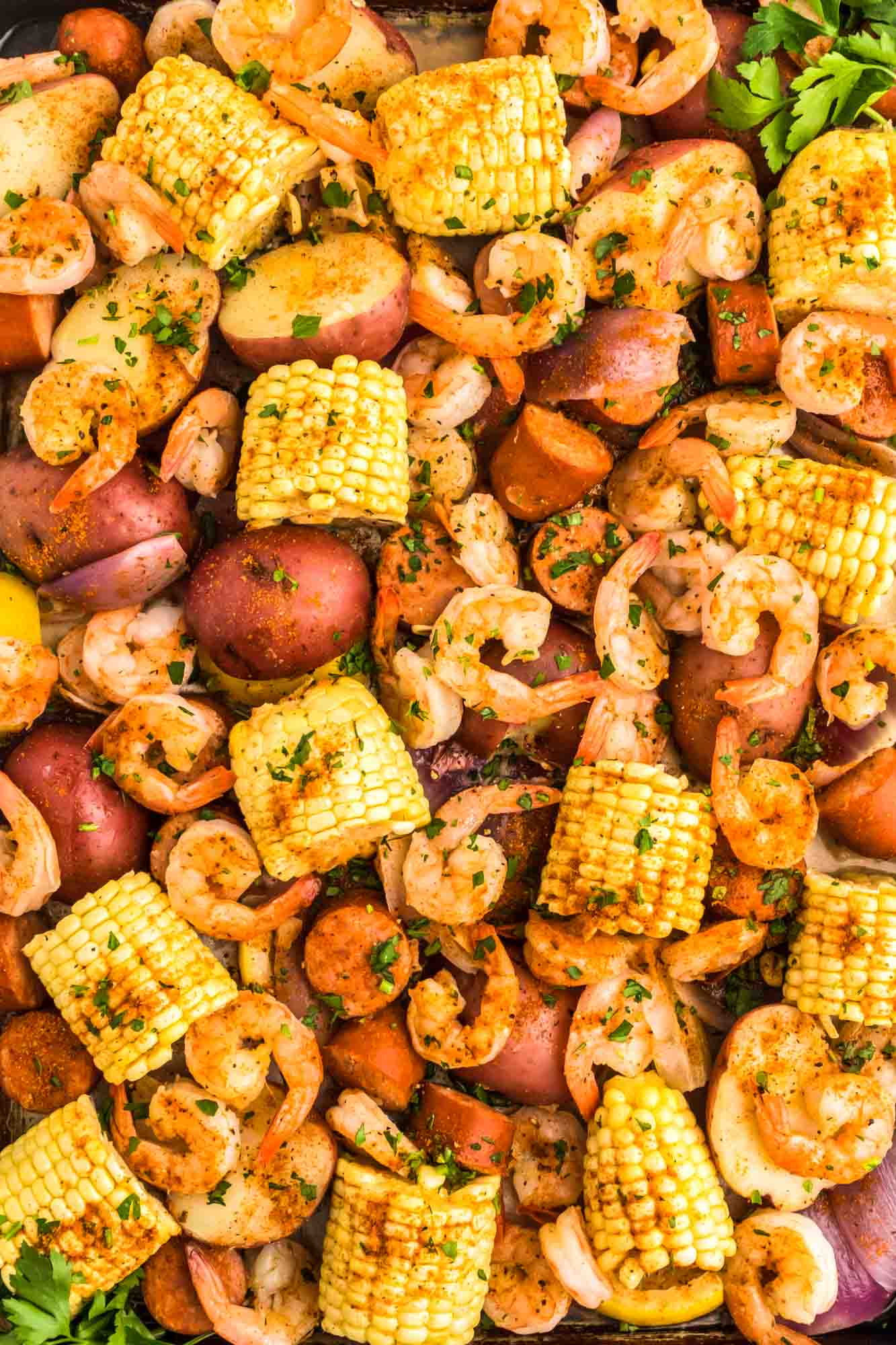 Overhead shot of shrimp boil including shrimp, corn, red potatoes, and onion. Served in a large sheet pan.