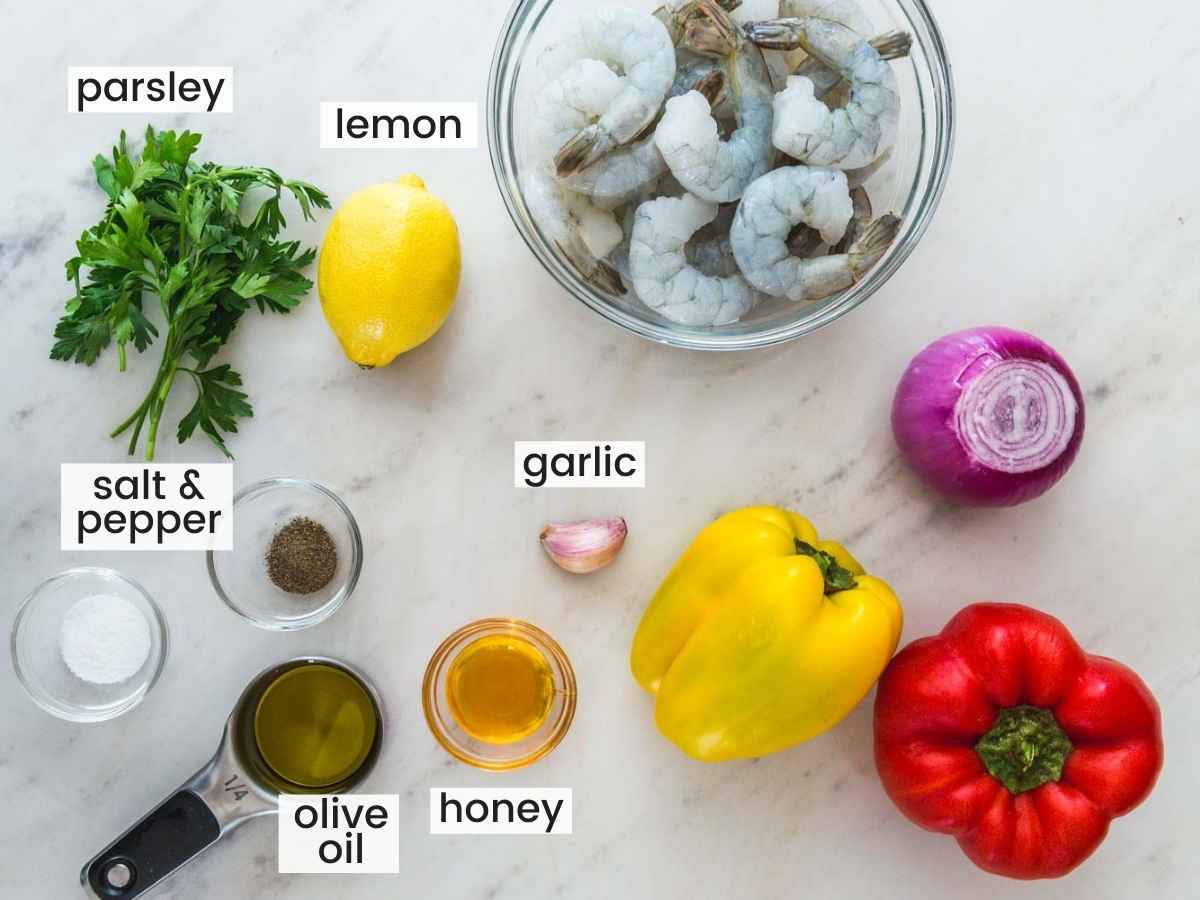 Ingredients needed to make grilled shrimp kabobs including shrimp, bell peppers, lemon, parsley, olive oil, honey, garlic, onion, salt and pepper.