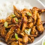 Slow Cooker Teriyaki Chicken served in a white bowl over rice, with toasted sesame seeds and sliced scallions