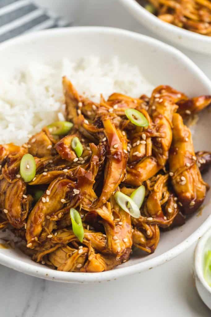 Slow Cooker Teriyaki Chicken served in a white bowl over rice, with toasted sesame seeds and sliced scallions