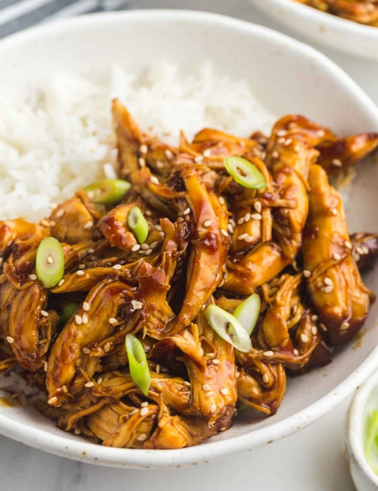 Slow Cooker Teriyaki Chicken served in a white bowl over rice, with toasted sesame seeds and sliced scallions