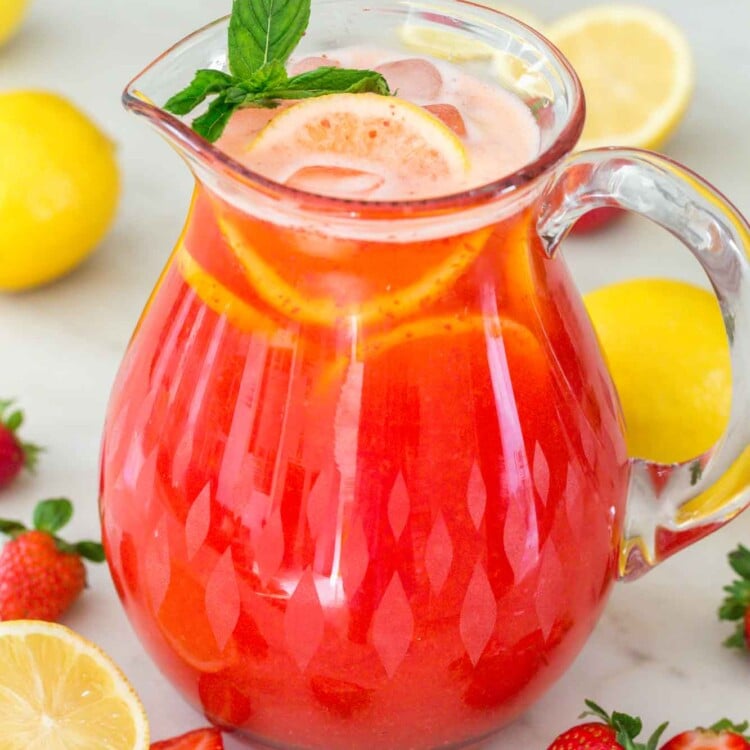Strawberry lemonade in a glass pitcher with fresh strawberries and fresh lemons