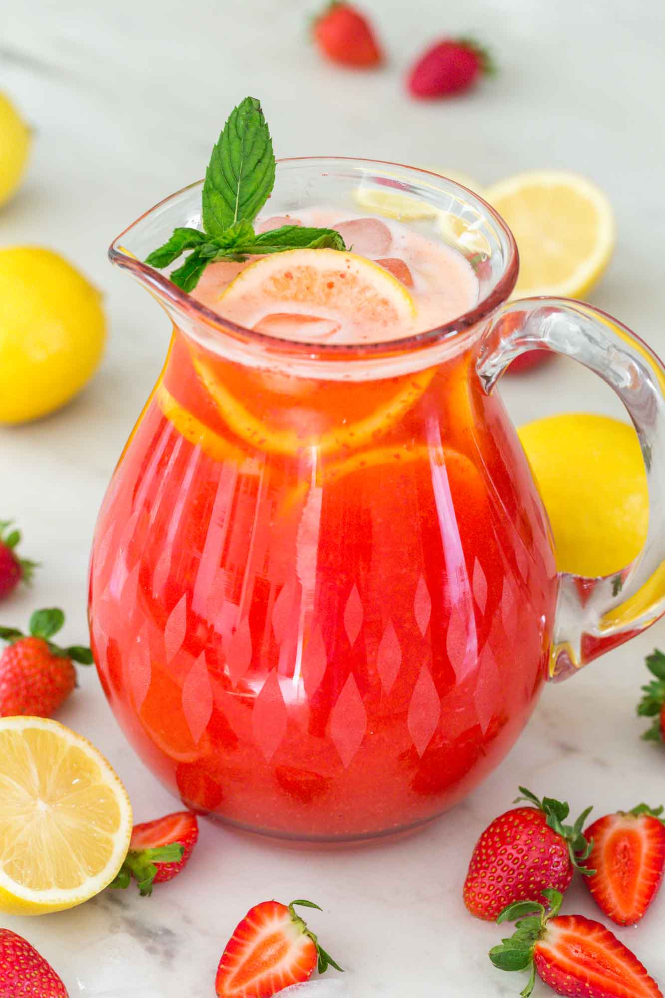 Strawberry lemonade in a glass pitcher with fresh strawberries and fresh lemons