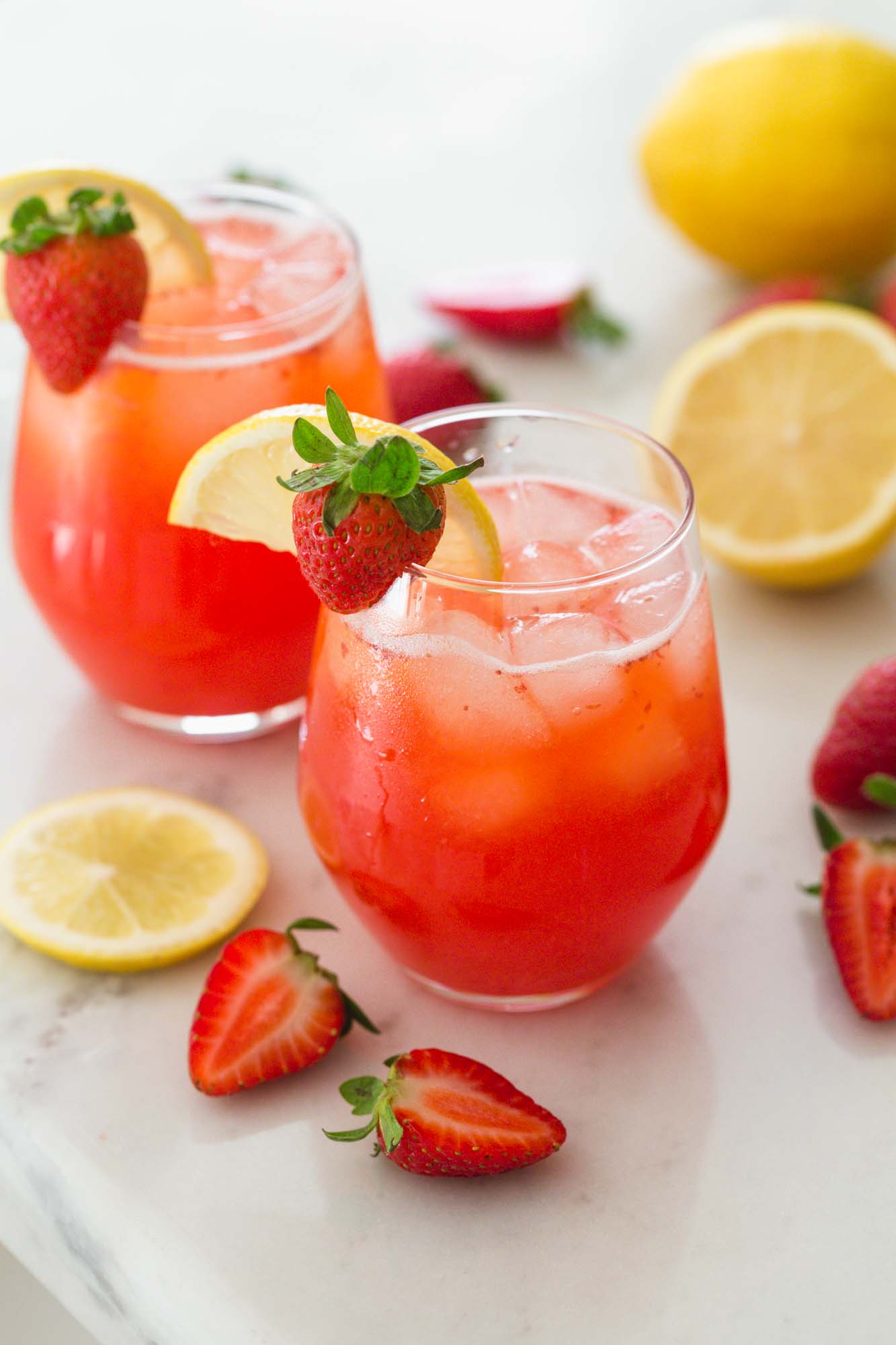 Chilled strawberry lemonade served with ice in two glasses, placed on a white marble counter