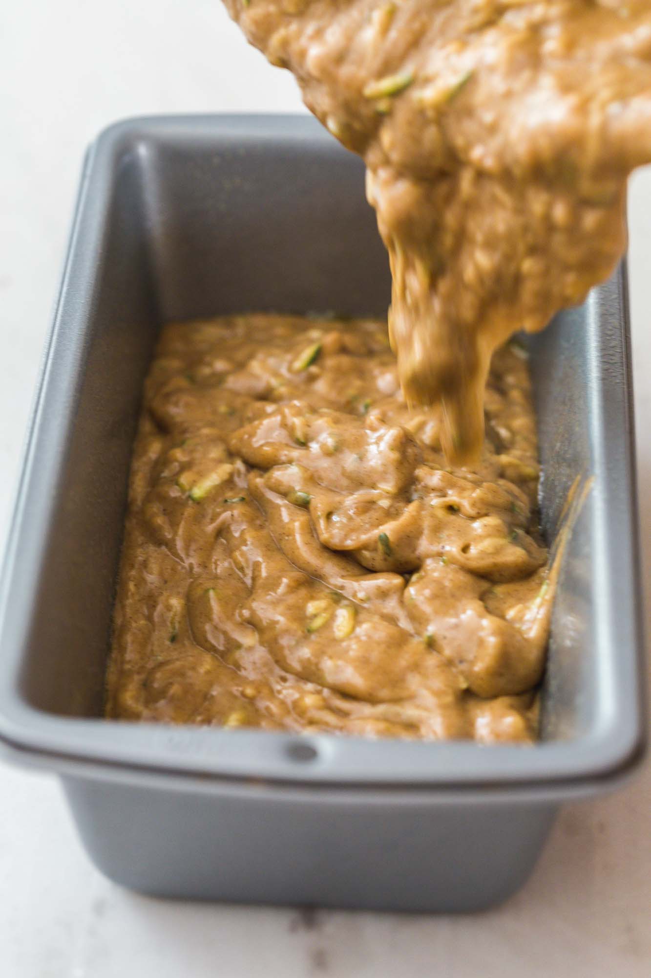 Pouring zucchini bread batter into a greased loaf pan