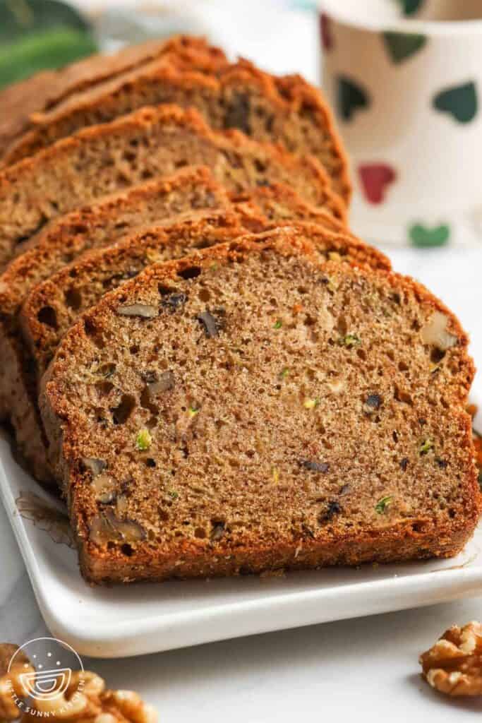 Slices of moist zucchini bread with walnuts on a white plate.