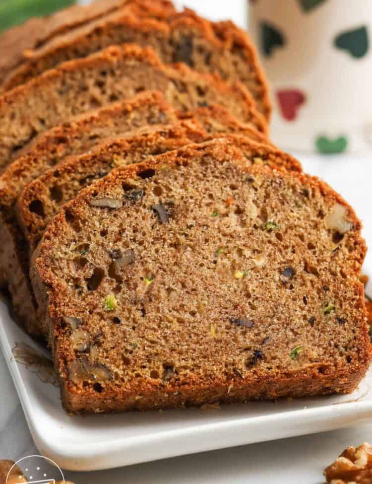 Slices of moist zucchini bread with walnuts on a white plate.