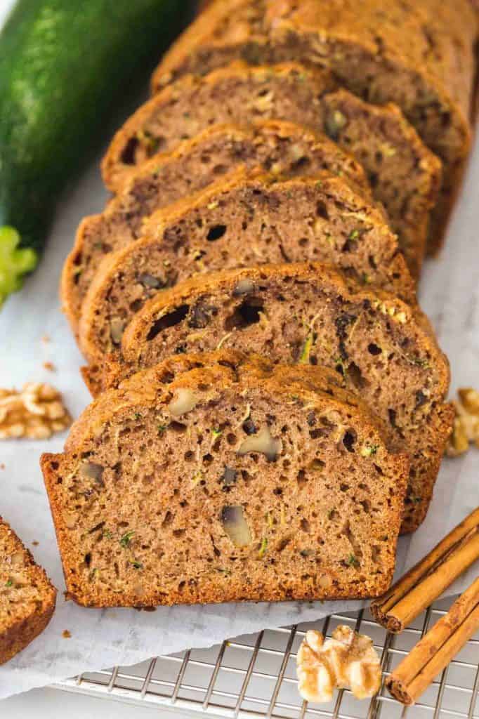 Sliced zucchini bread on a wire rack with a green zucchini in the background