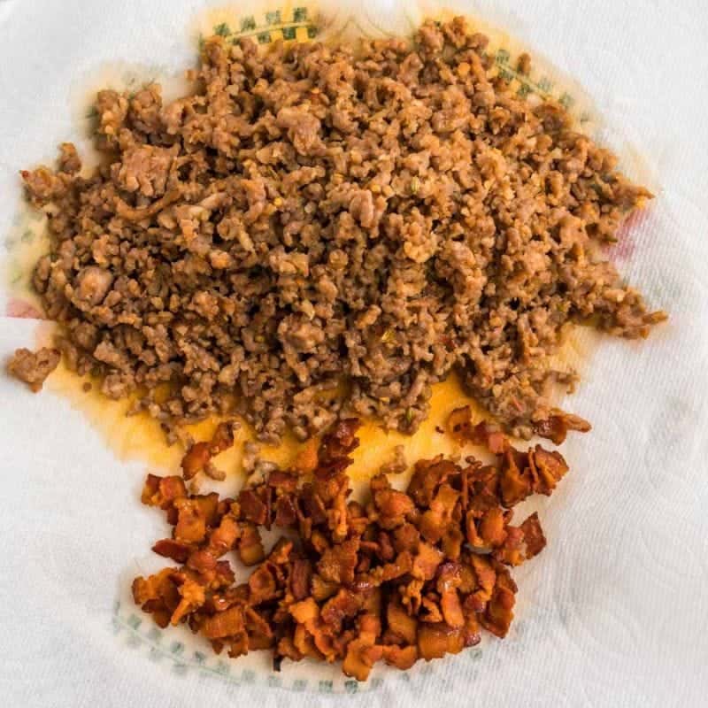 Cooked Italian sausage and crispy chopped bacon on a plate after browning in a pot