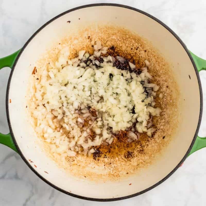 Diced onion cooking in a Dutch oven with browned bits from sausage and bacon