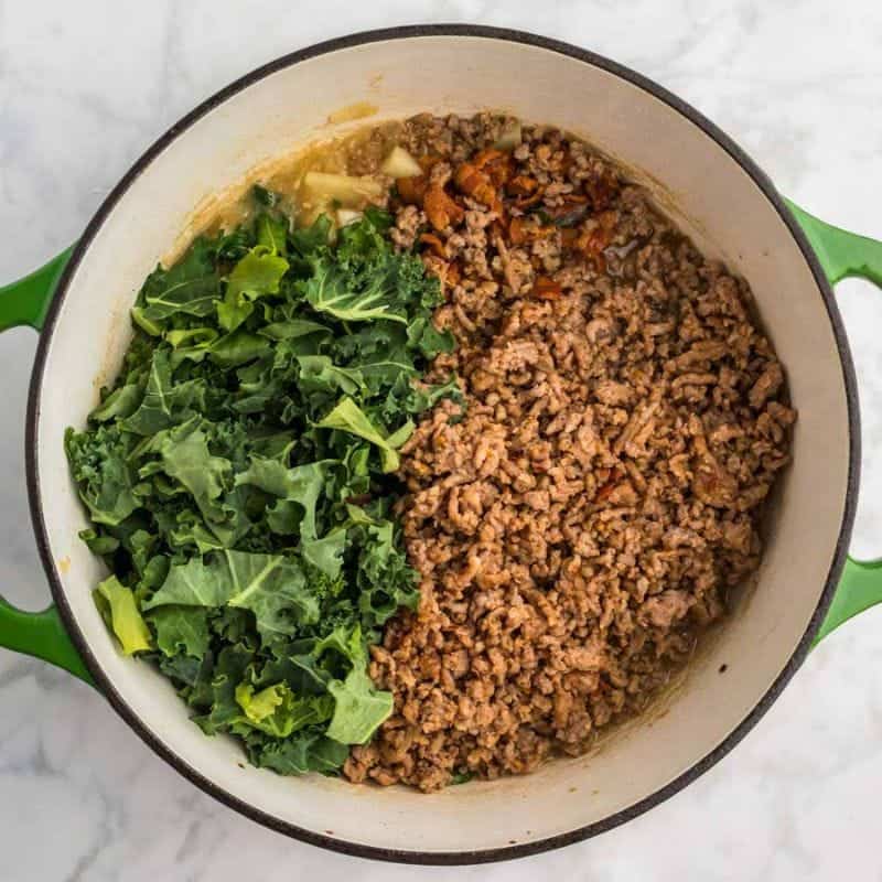 Cooked sausage, chopped kale, and bacon added to soup in a Dutch oven