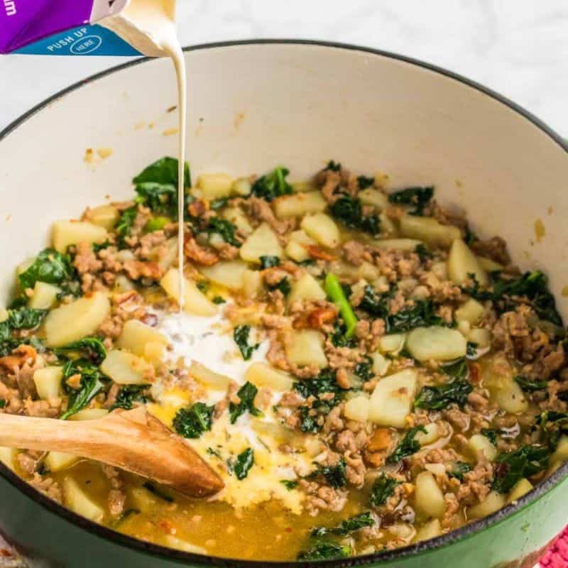 Pouring cream into Zuppa Toscana soup with sausage, potatoes, and kale