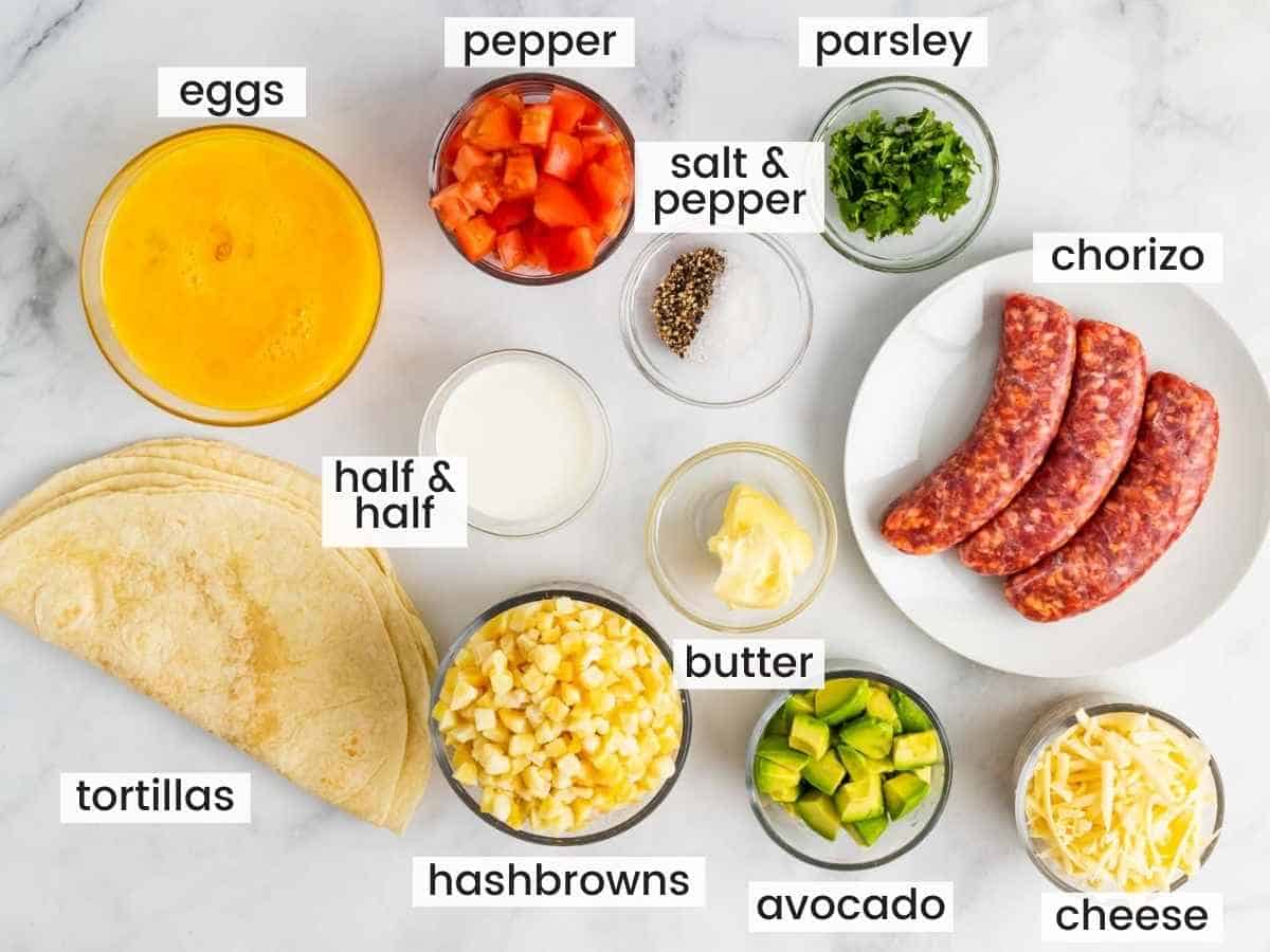 Ingredients needed for making breakfast burritos including sausage, tortillas, hashbrowns, eggs, bell pepper, avocado, butter, cheese, parsley, half and half, and salt and pepper.