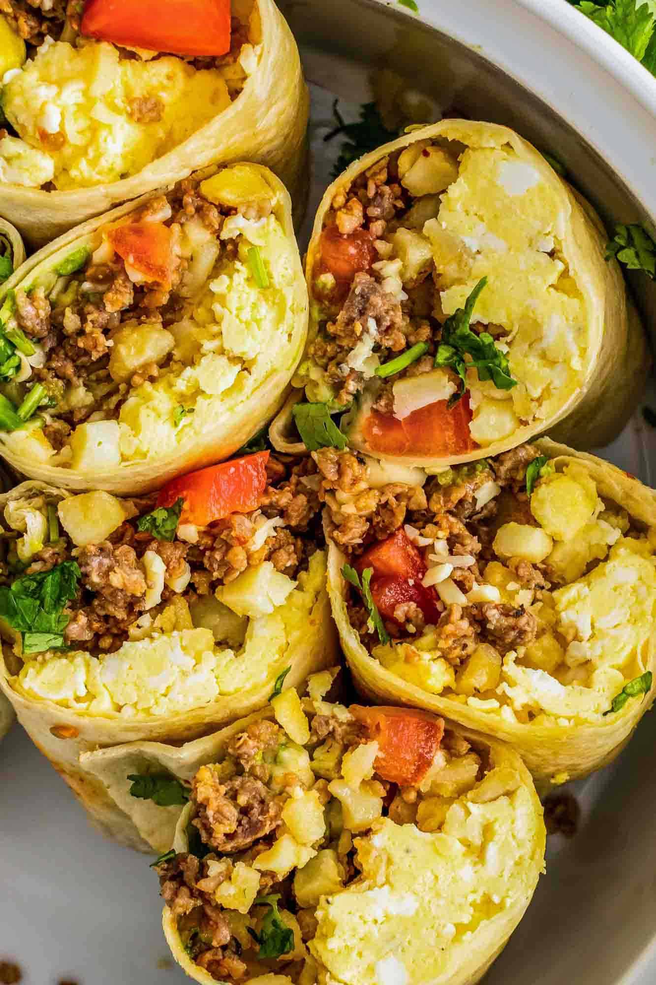 Six breakfast burrito halves placed in a large bowl, cut facing the camera
