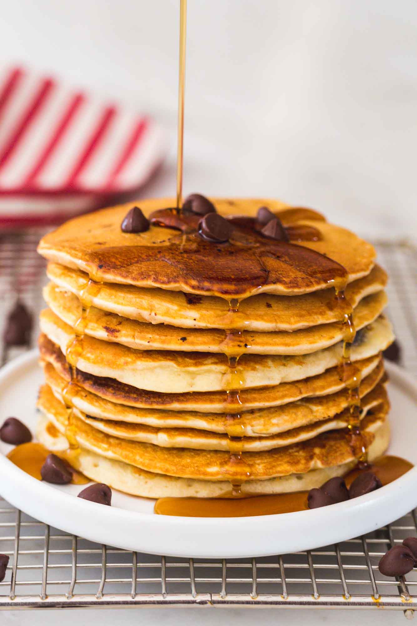 Drizzling pancake syrup over a stack of chocolate chip pancakes