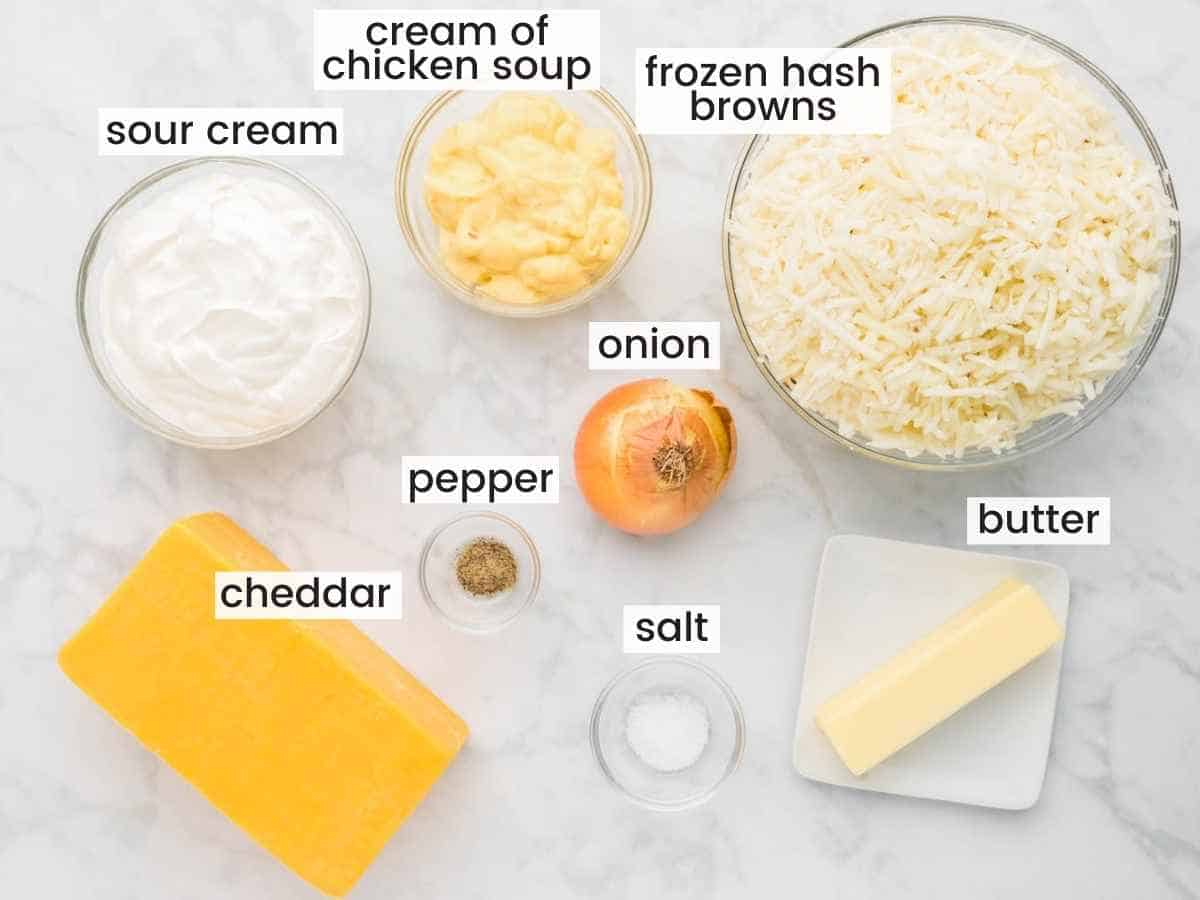 Ingredients needed to make Cracker Barrel Hashbrown Casserole inclduing hash browns, cheddar, sour cream, onion, butter, cream of chicken soup, salt, and pepper.