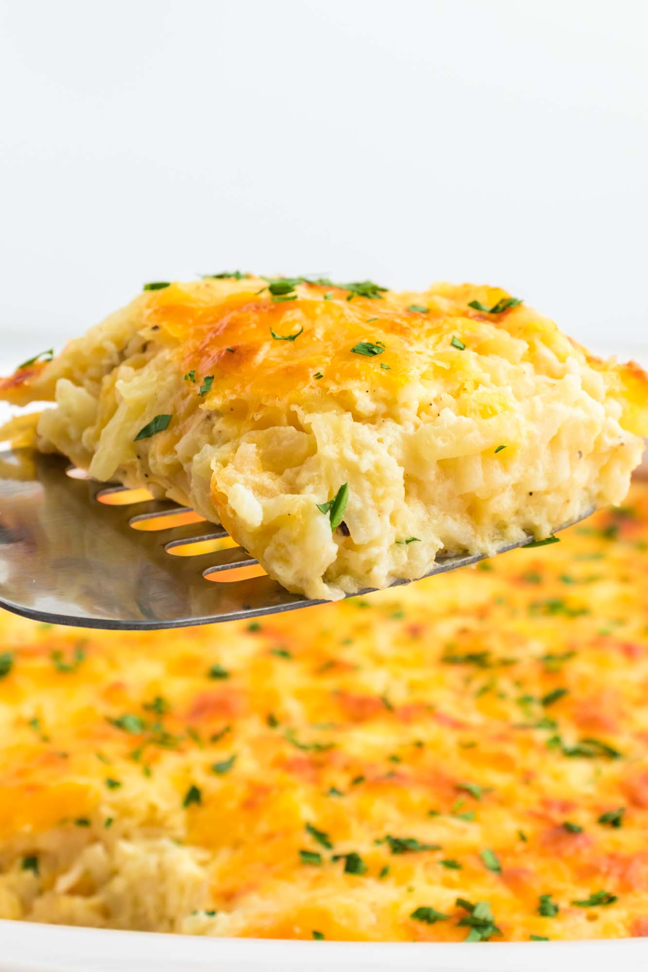 A slice of cheesy casserole being served from the casserole dish