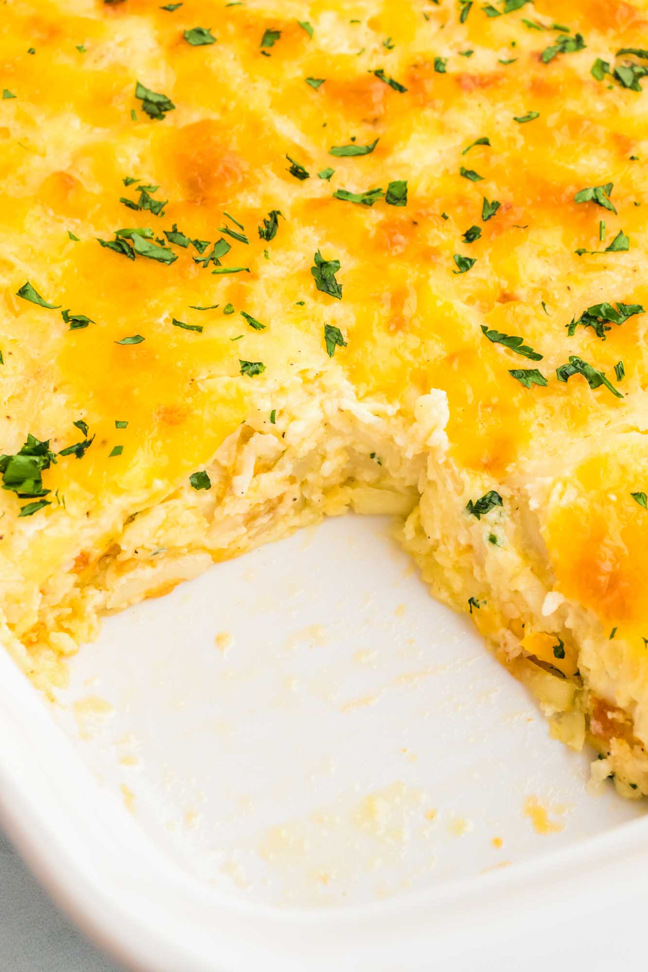 Close up of cheesy hashbrown casserole in a white casserole dish.