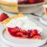 A slice of strawberry pie placed on a white plate, and a whole pie in the background