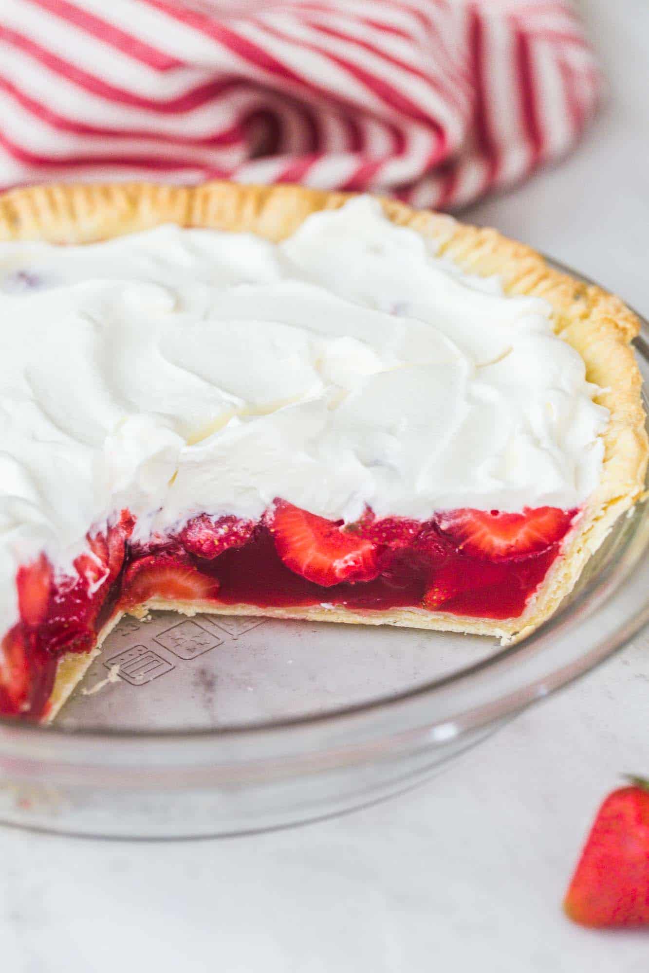 Whole strawberry pie in a pie dish, topped with whipped cream