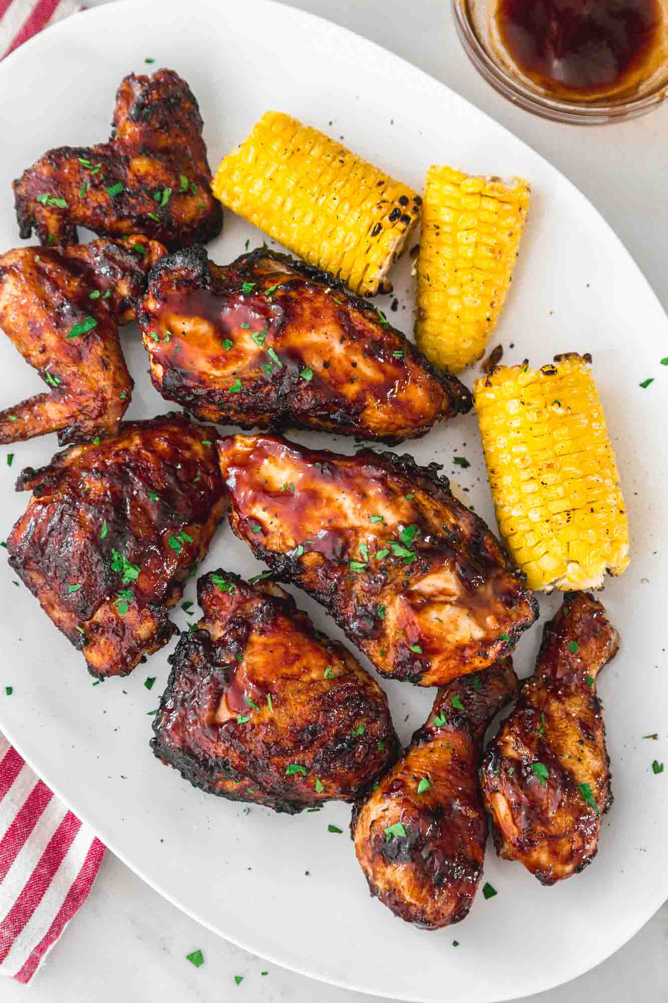 Grilled BBQ chicken on a white platter, served with grilled corn on the side