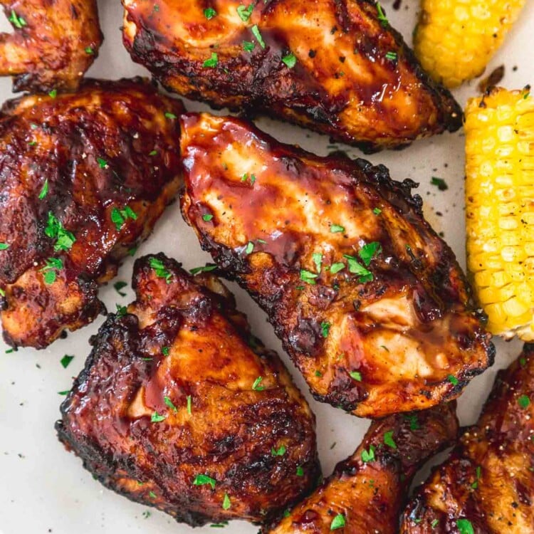 Grilled BBQ chicken served on a white platter with corn on the cob on the side