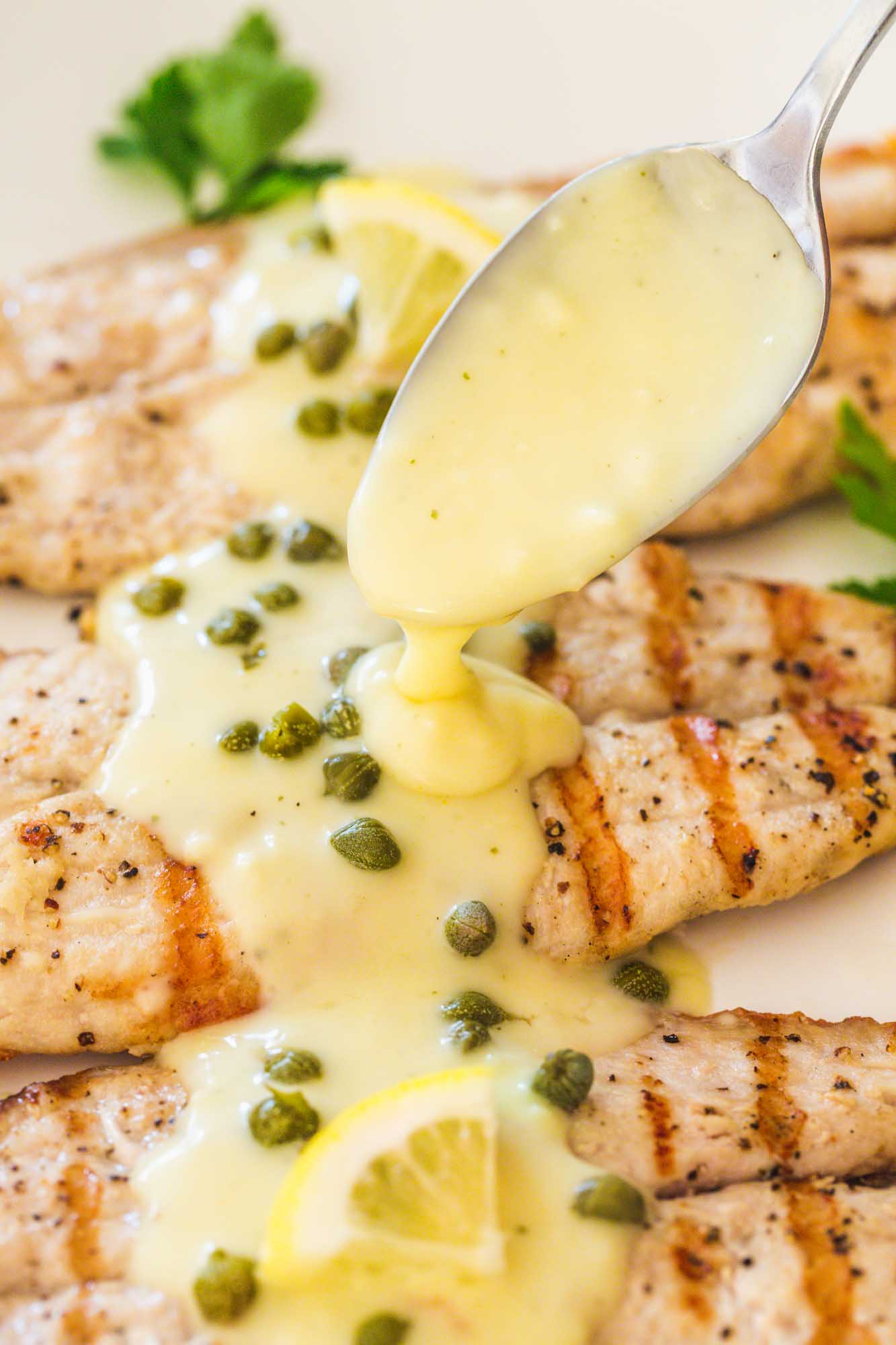 Spooning creamy piccata sauce over grilled tilapia