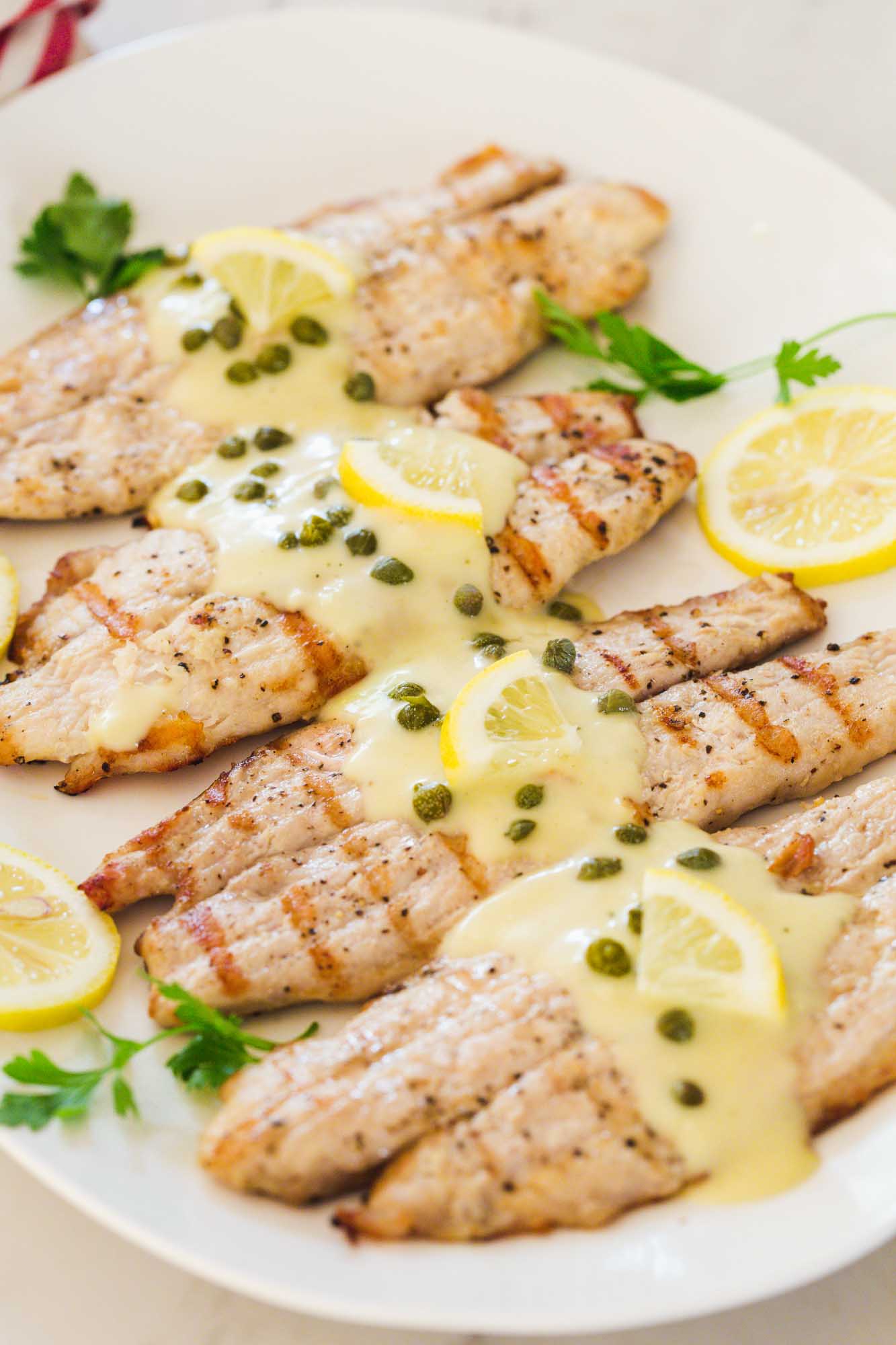 Grilled tilapia served on a platter, and topped with piccata sauce, capers and fresh lemon slices.