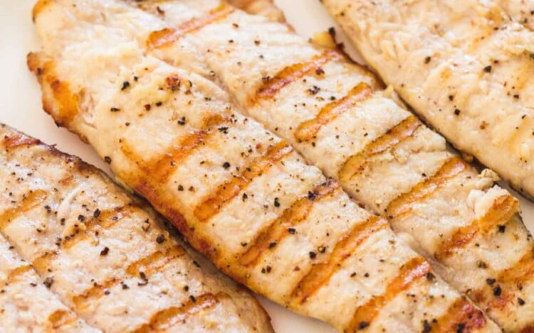 Grilled tilapia fillets served on a large white platter with fresh lemon slices and parsley