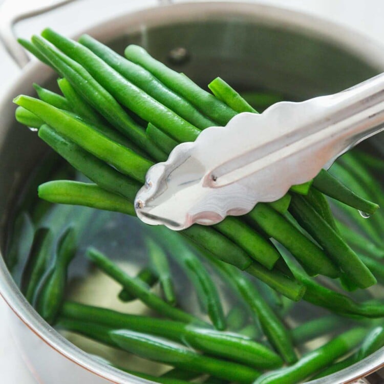 Taking blanched green beans with tongs from a saucepan