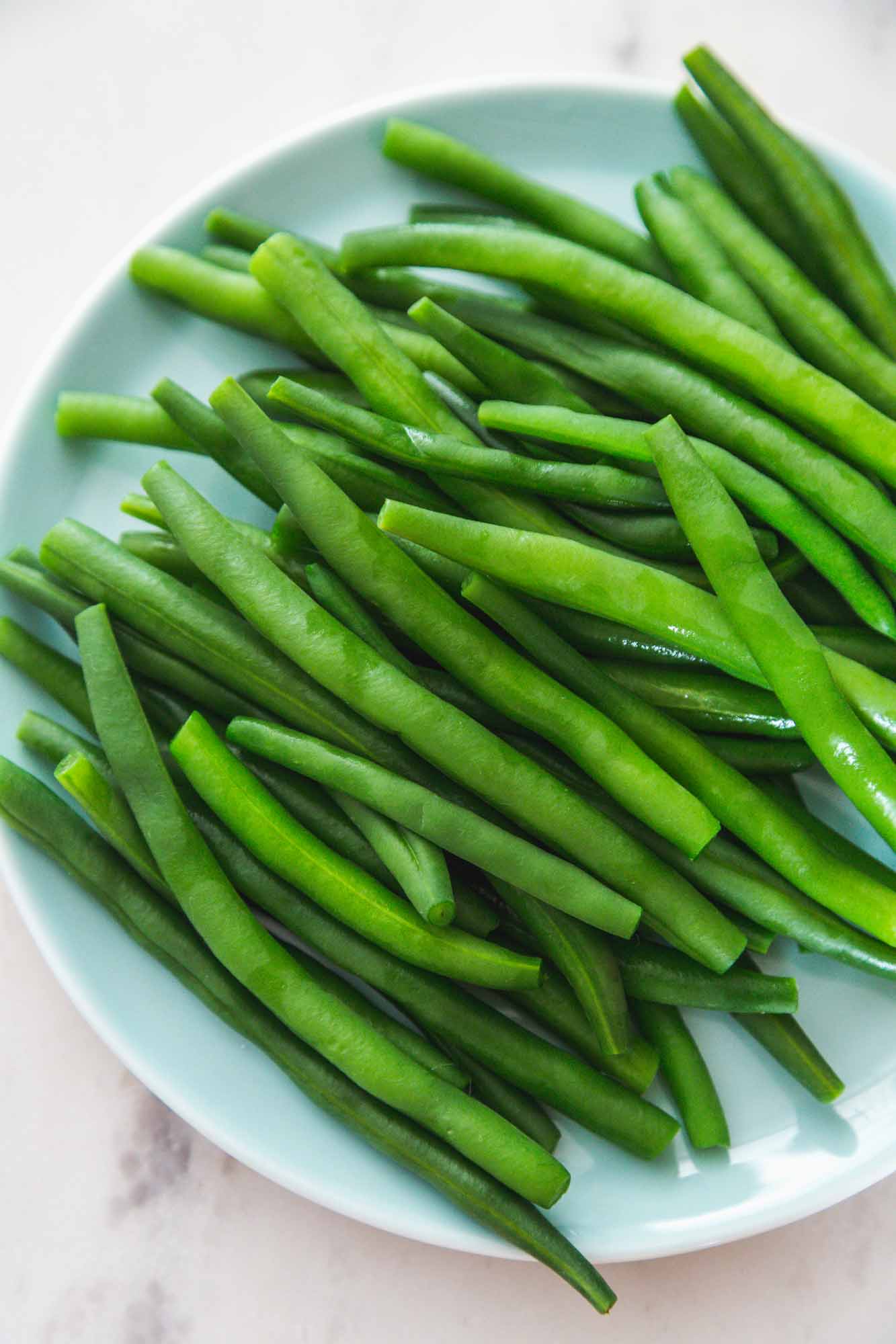Overhead shot of blanched green beans on a blue side plate