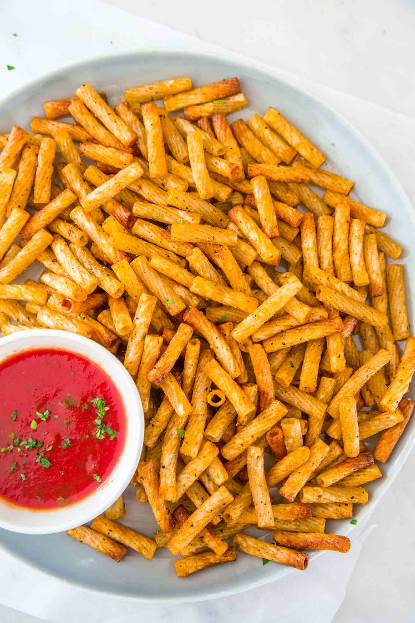 Pasta chips served on a large plate, with a tomato dip on the side.