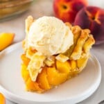 Slice of peach pie on a small white plate with a scoop of ice cream