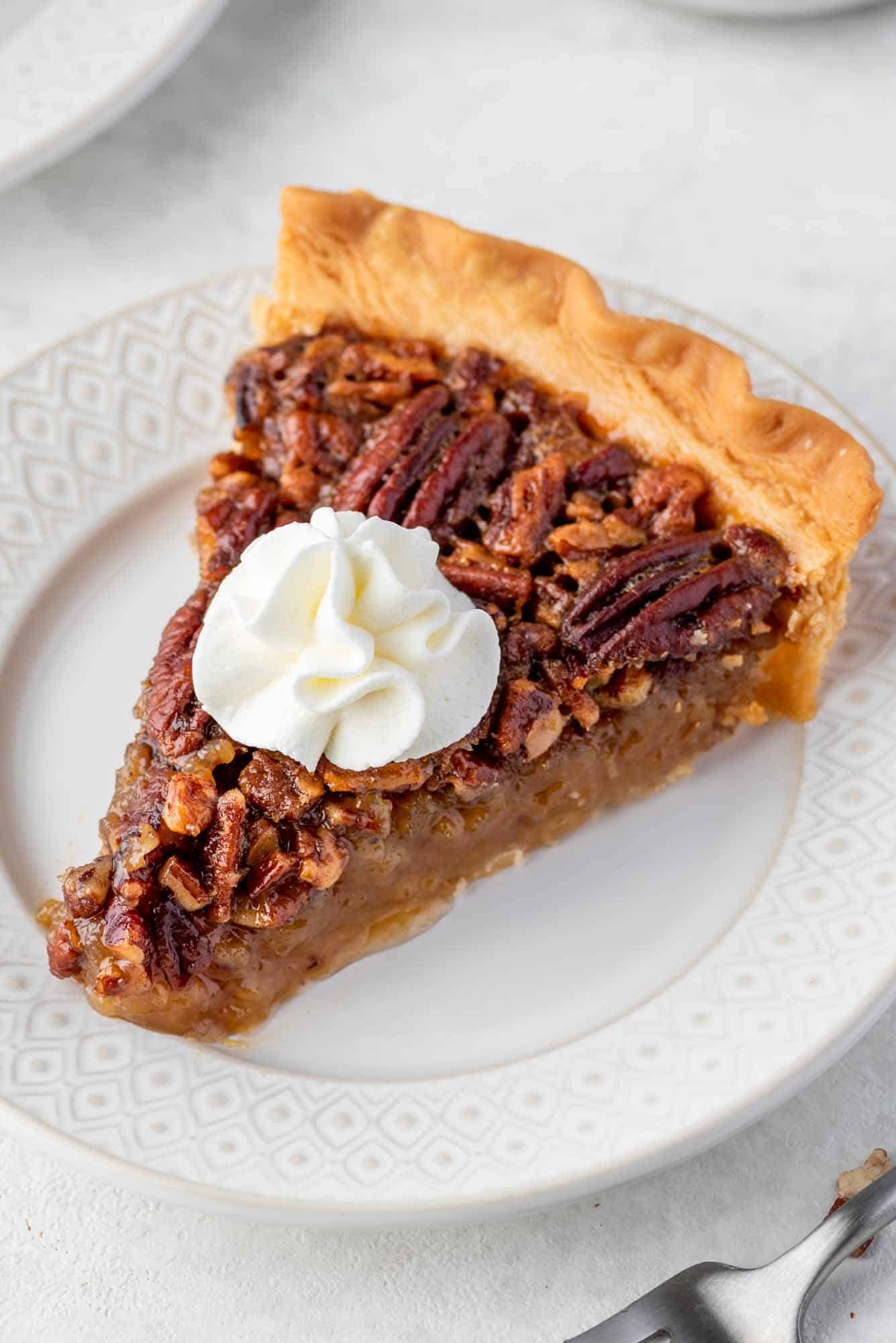 A slice of Pecan pie served on a white plate and topped with whipped cream.