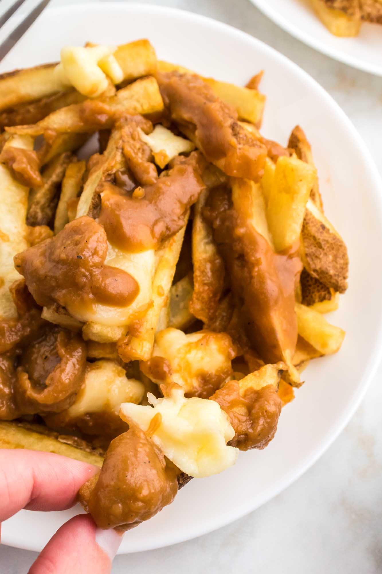 Taking a poutine fry with cheese and gravy from a plate
