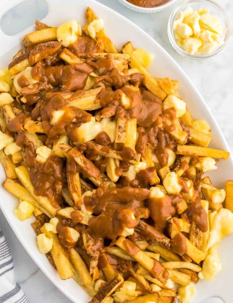 Poutine served on a large platter, with cheese curds and extra gravy on the side.
