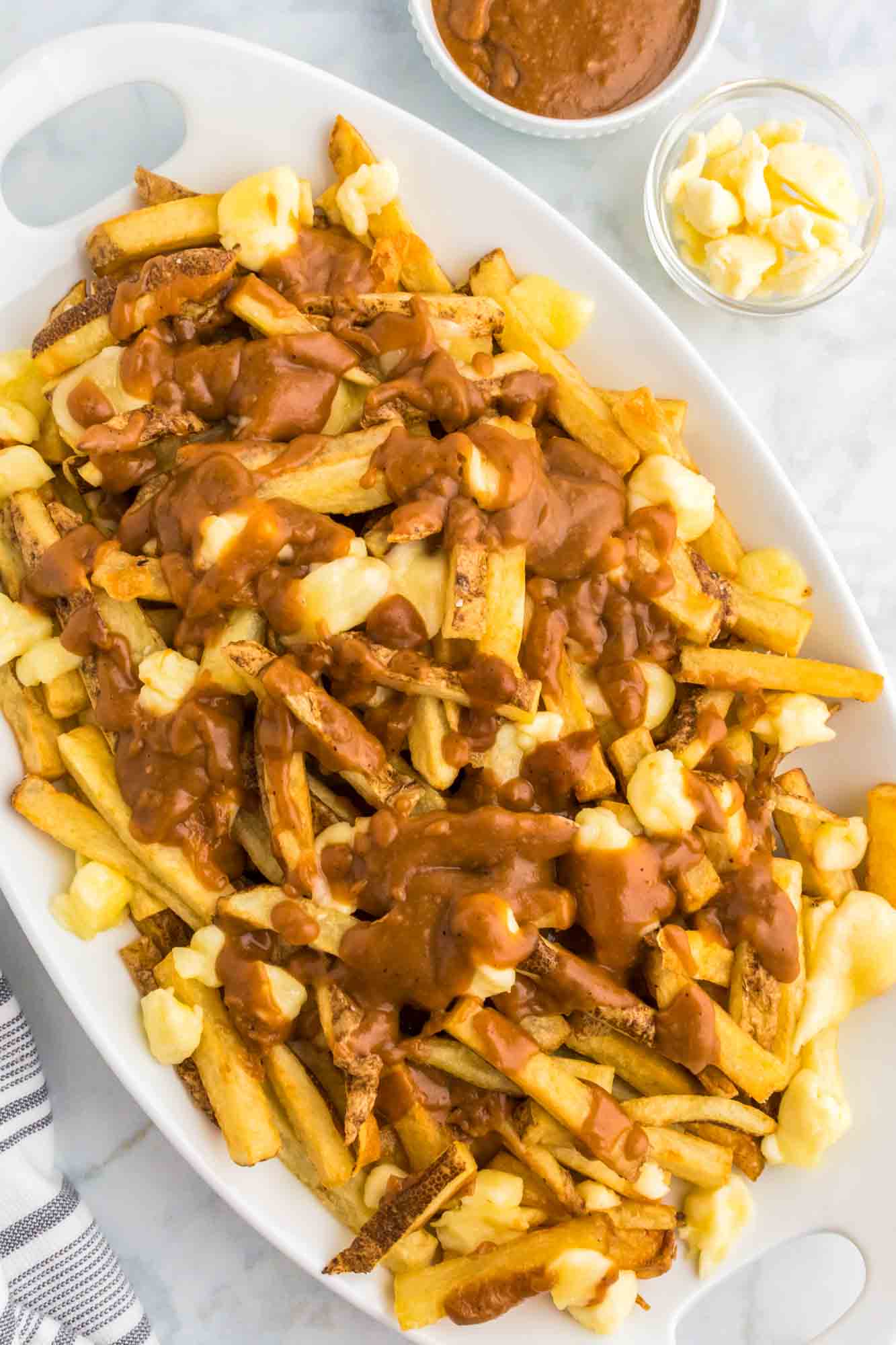 Poutine served on a large platter, with cheese curds and extra gravy on the side.