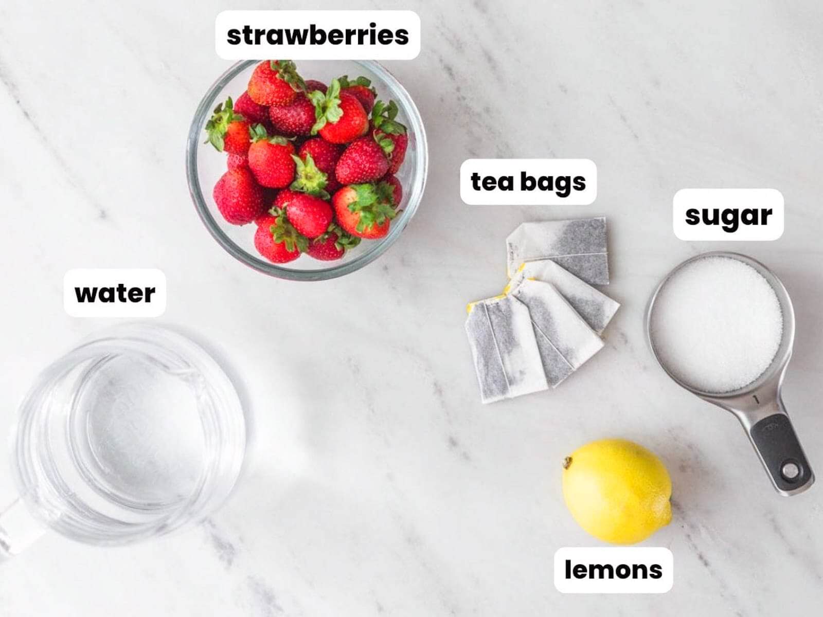 Fresh strawberries, black tea bags, sugar, lemon, and water arranged for homemade strawberry iced tea.