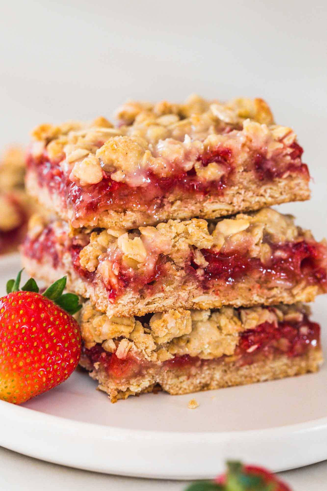 Strawberry Oatmeal Bars stacked on each other, with fresh strawberry on the side