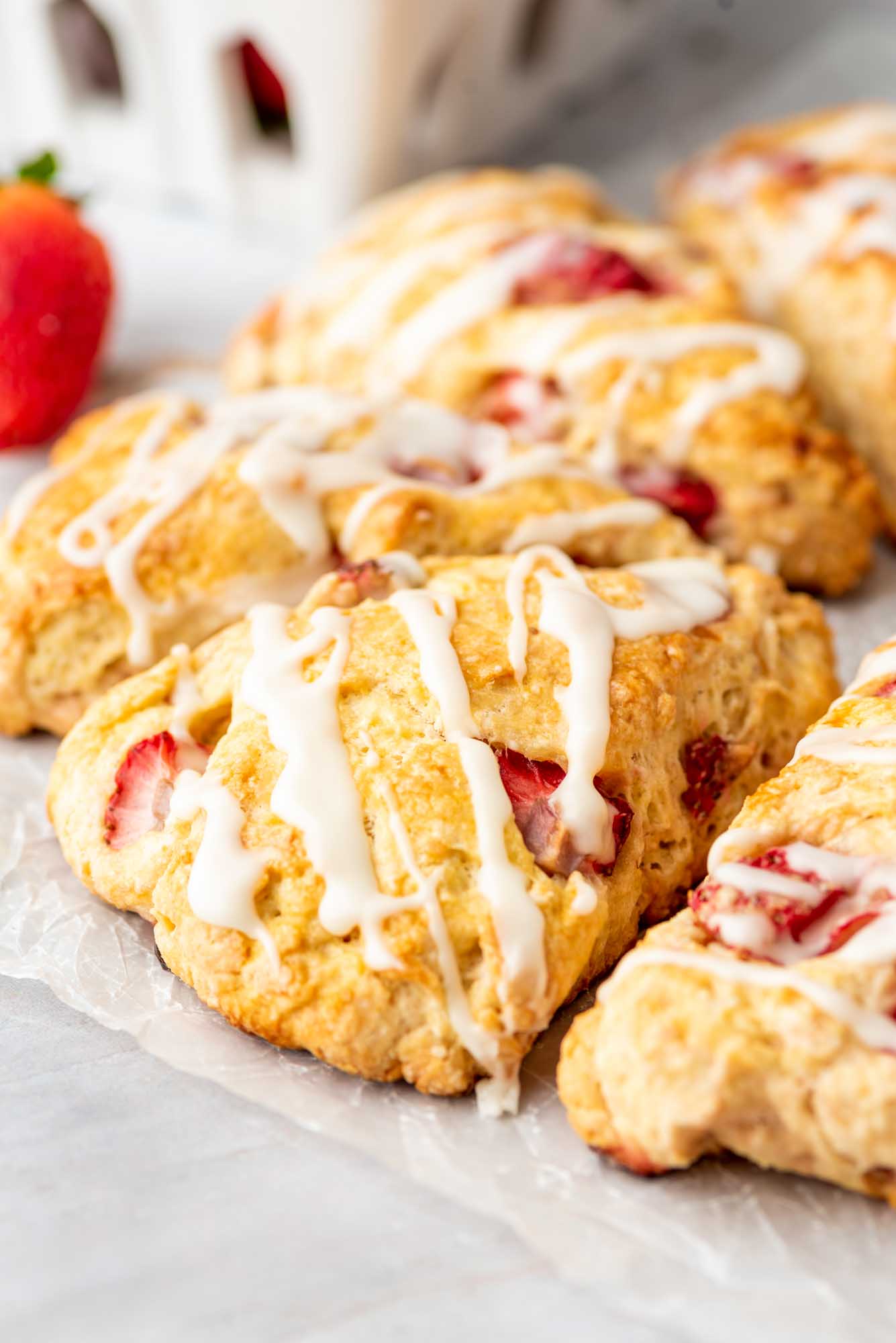 Straberry scones with white vanilla drizzle, and fresh strawberry in the background