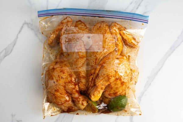 Spatchcocked chicken marinating with lime in a sealed plastic bag