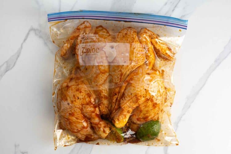 Spatchcocked chicken marinating with lime in a sealed plastic bag