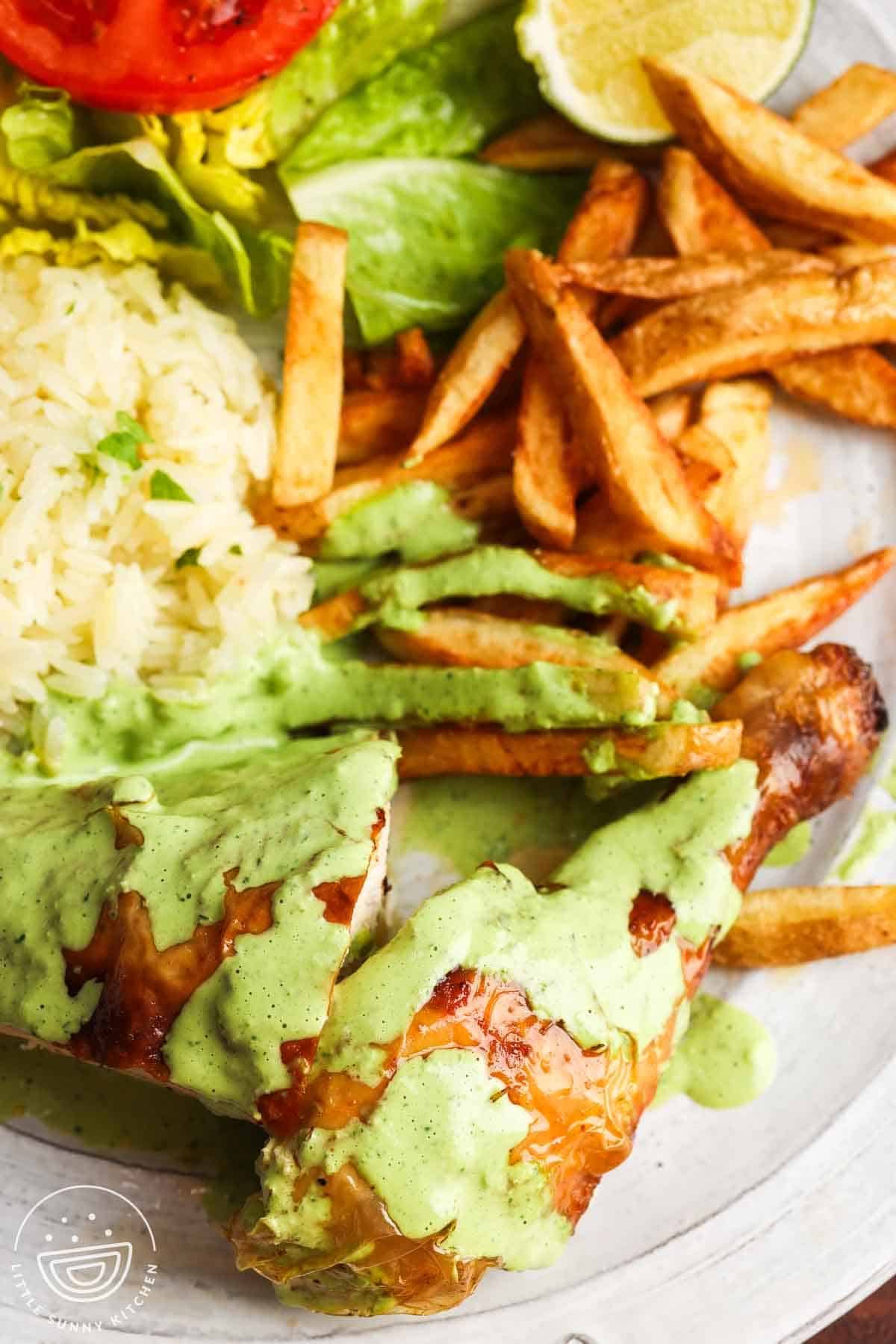 Peruvian chicken drizzled with green sauce, served with rice, fries, lettuce, tomato, and lime.