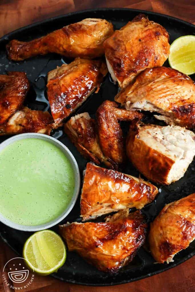 Roasted Peruvian chicken pieces served on a black platter with green sauce and lime wedges.