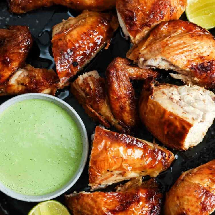 Roasted Peruvian chicken pieces served on a black platter with green sauce and lime wedges.